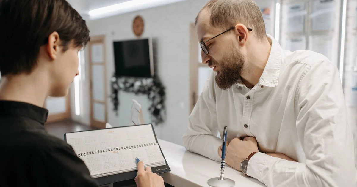 Recepcionista mostrando agenda em papel para paciente no balcão da clínica