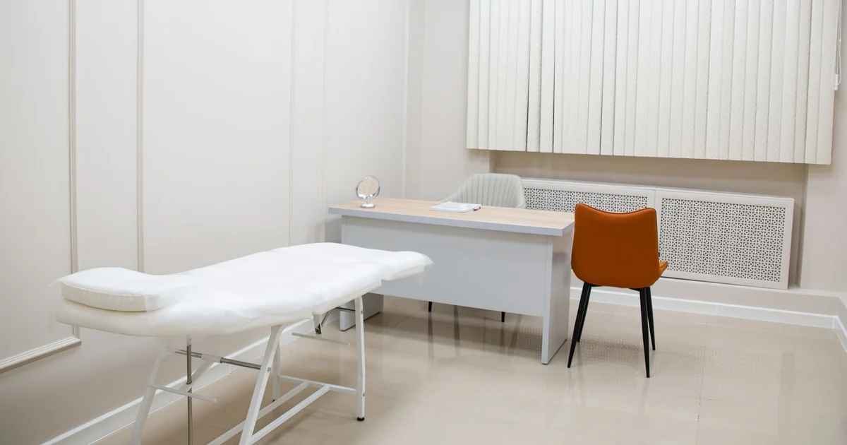Sala de atendimento vazia com maca, mesa e cadeiras em clínica