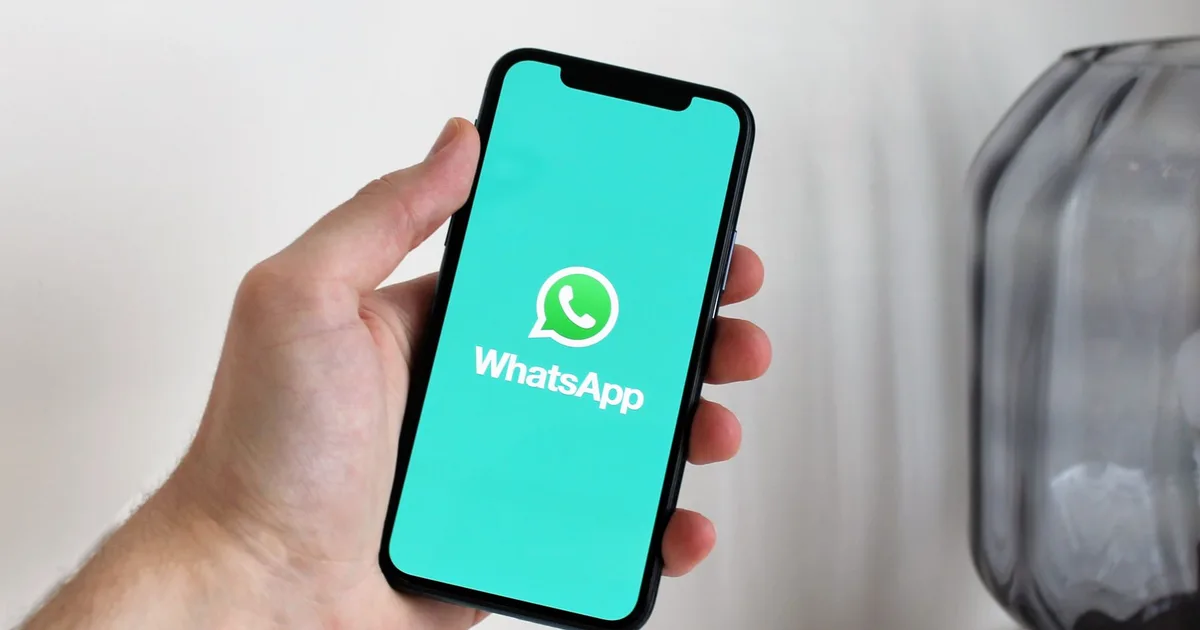 Mão segurando um celular com o ícone do WhatsApp na tela